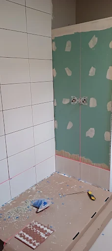 Douche en travaux : un mur carrelé de faïence blanche, le mur du fond pas encore carrelé