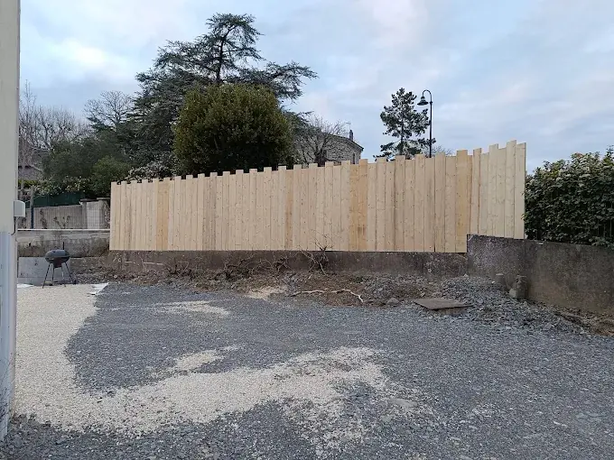 Palissade en bois clair neuve, montée sur un muret, devant un terrain en gravier