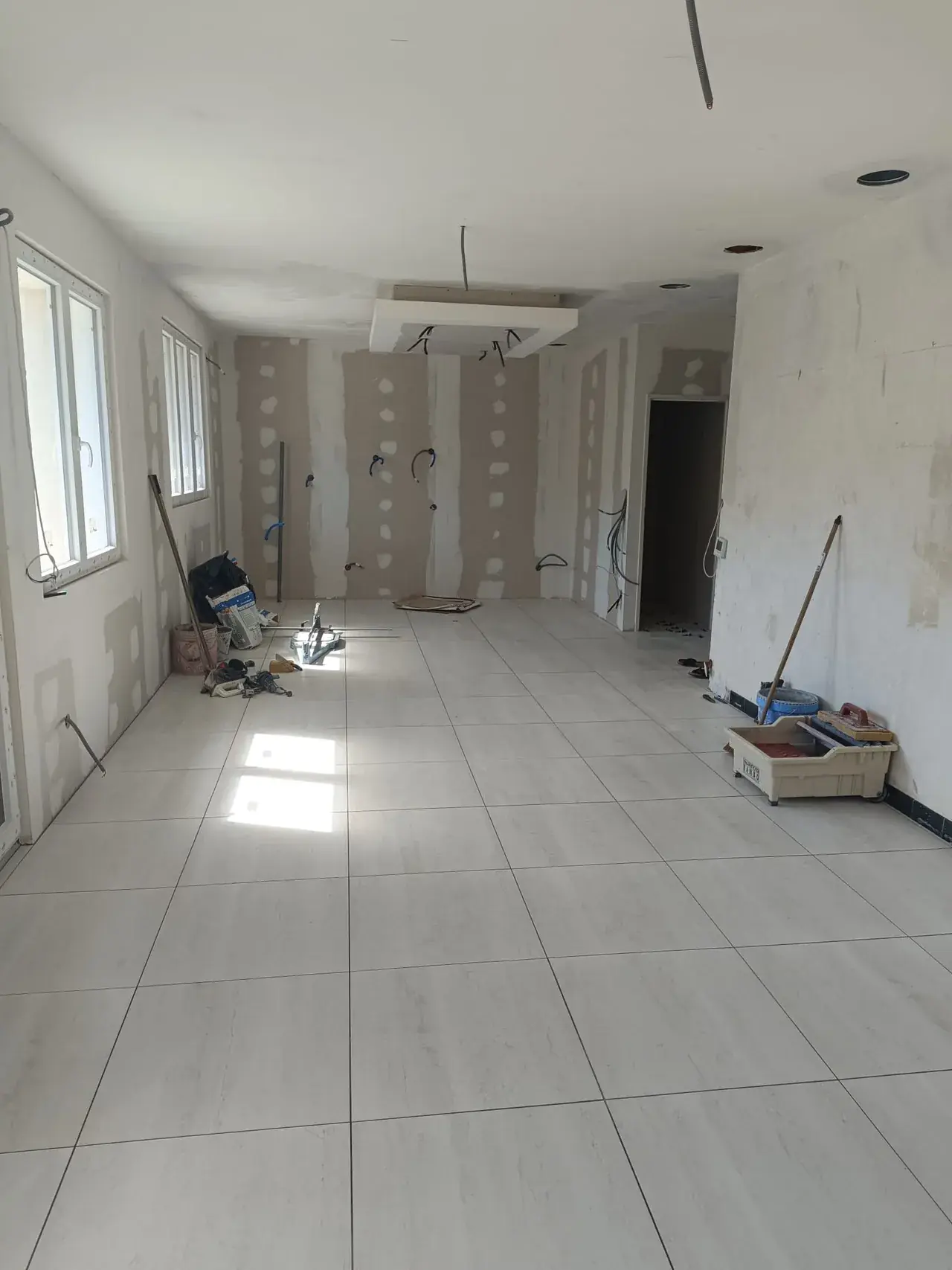 Pièce en travaux : grand carrelage clair posé, plaques de plâtre aux joints enduits, tuyaux et gaines en attente