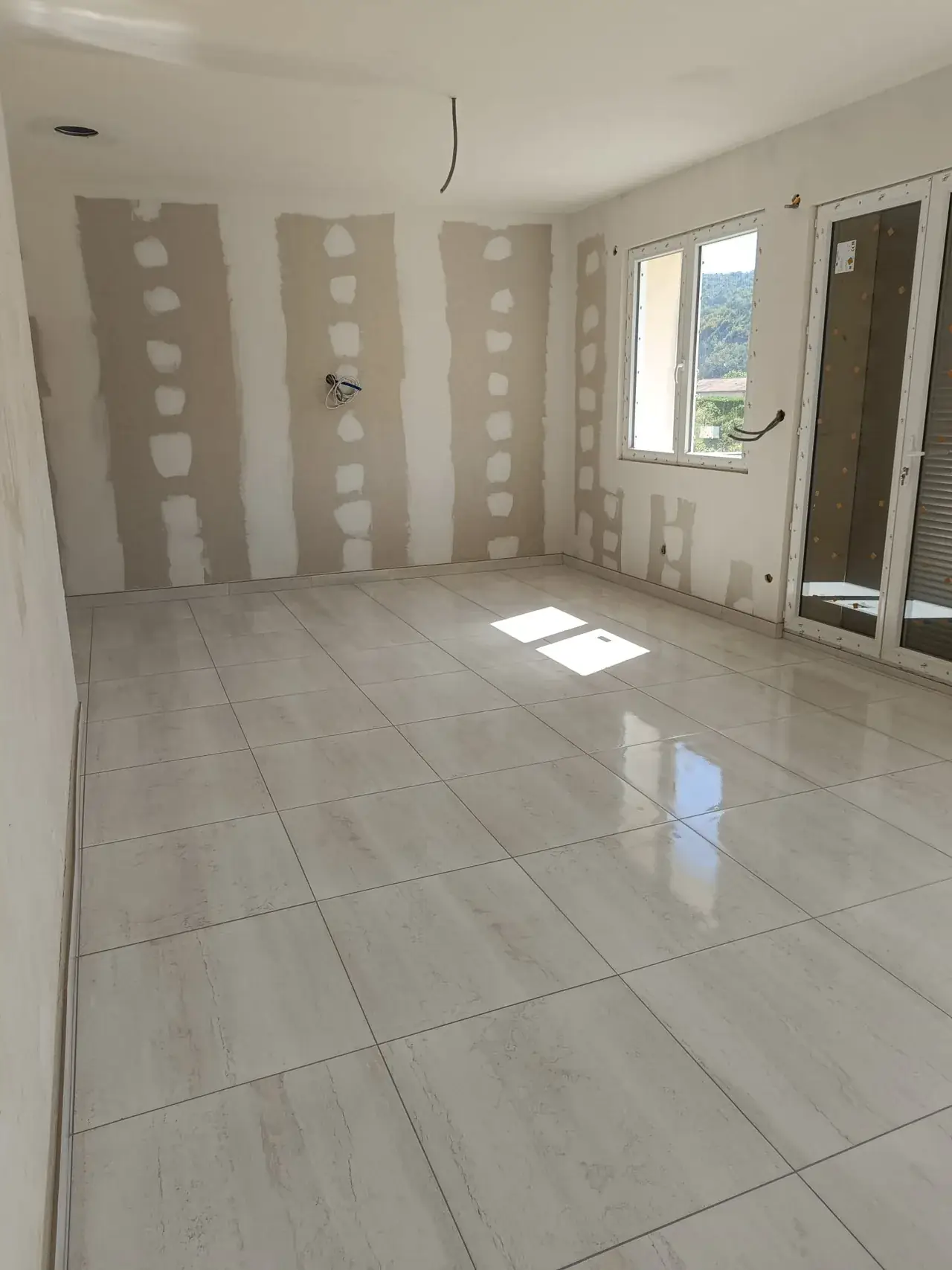 Pièce aux murs en plaques de plâtre, joints et têtes de vis enduits, grand carrelage clair posé avec ses plinthes