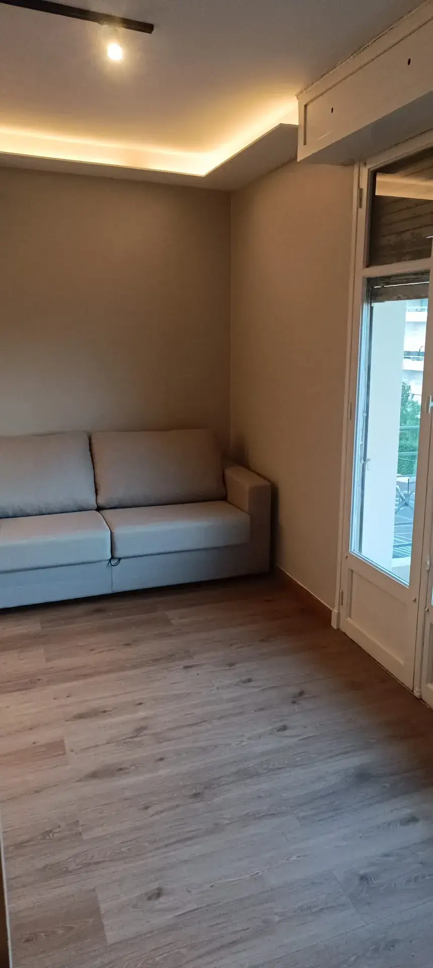 Pièce à vivre : canapé clair dans l'angle, faux plafond à bandeau lumineux, sol en lames de teinte bois