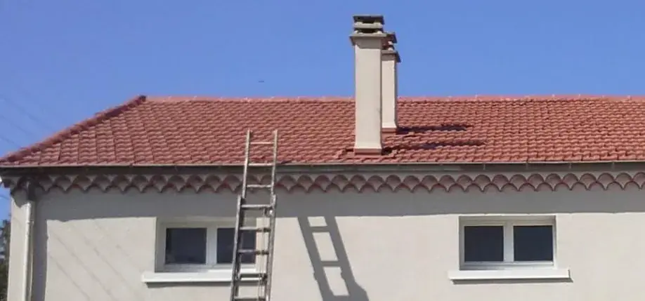 Toit de tuiles rouges sous un ciel sans nuage, bordé d’une génoise ; une échelle dressée dépasse le bord du toit