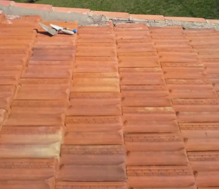 Pan de tuiles orangées bordé d'un bandeau de mortier gris, lisse à gauche, effrité à droite, sous un rang orangé ; deux truelles posées sur les tuiles