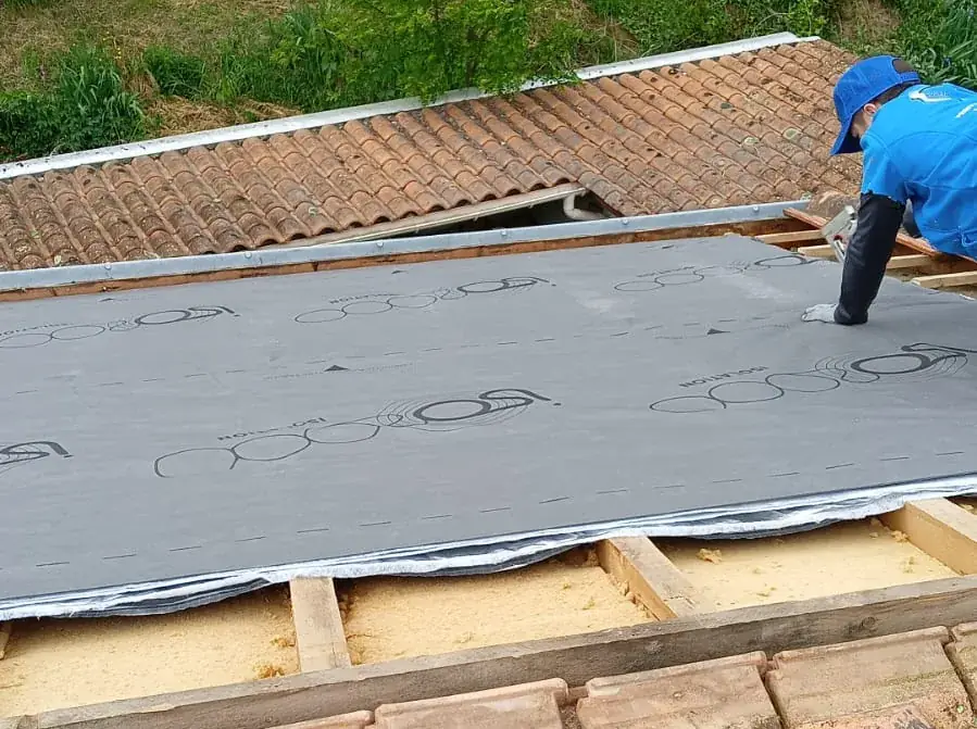 Écran de sous-toiture gris agrafé sur une pente de toit, panneaux isolants visibles sous le bord